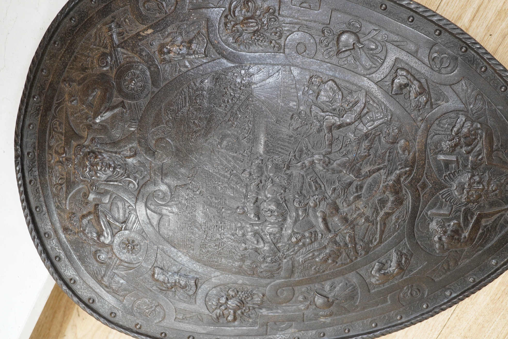 A decorative late 19th century cast iron shield in a romantic style, scene incorporates classical battles surrounded by masks captives, cannon and fruit, 60 x 42.5cm. Condition - good
